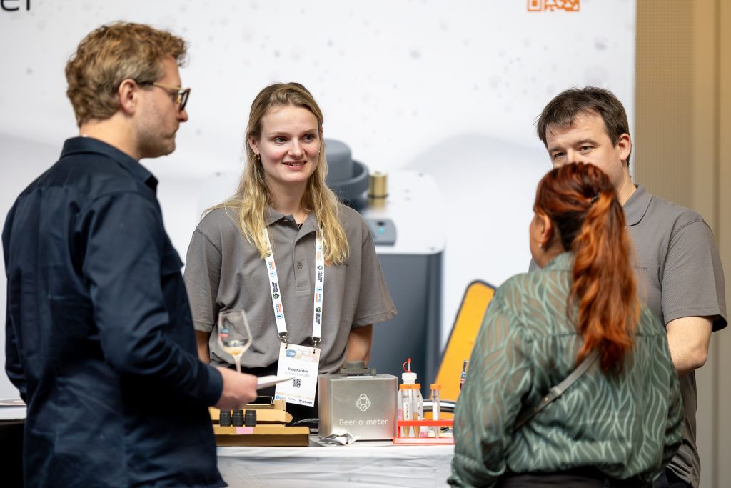 Beer-o-Meter team talking with visitors at a conference booth, demonstrating quality control tools and beer testing equipment